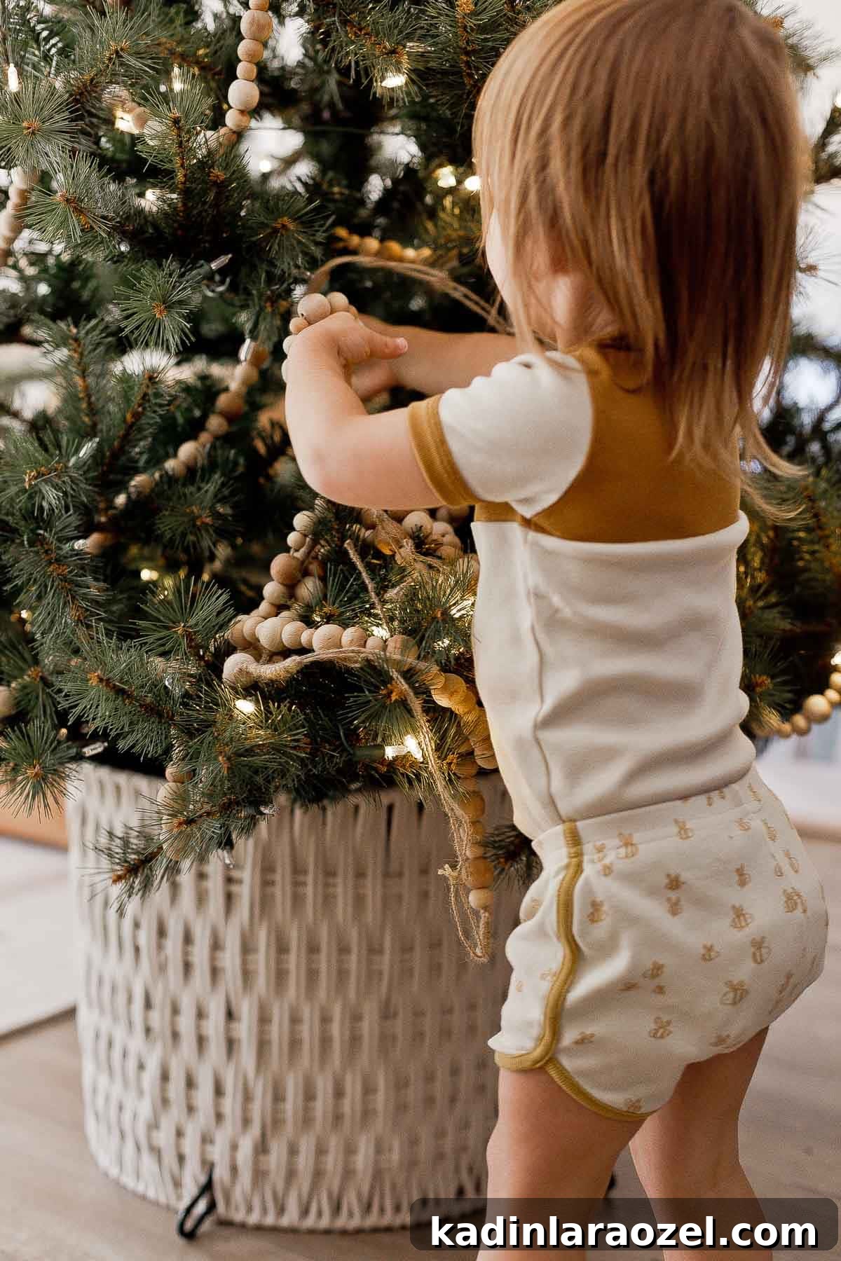Child decorating a Christmas tree with wood garlands.