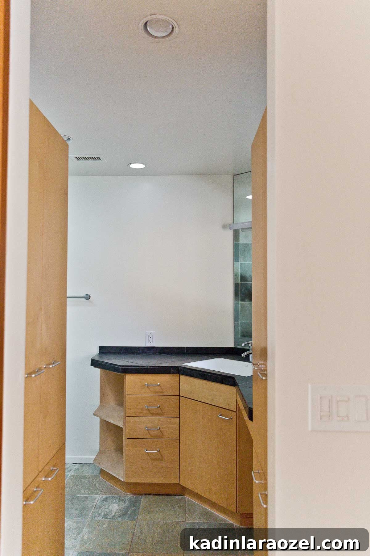 Photo of empty bathroom with wood cabinets and black natural stone counters.
