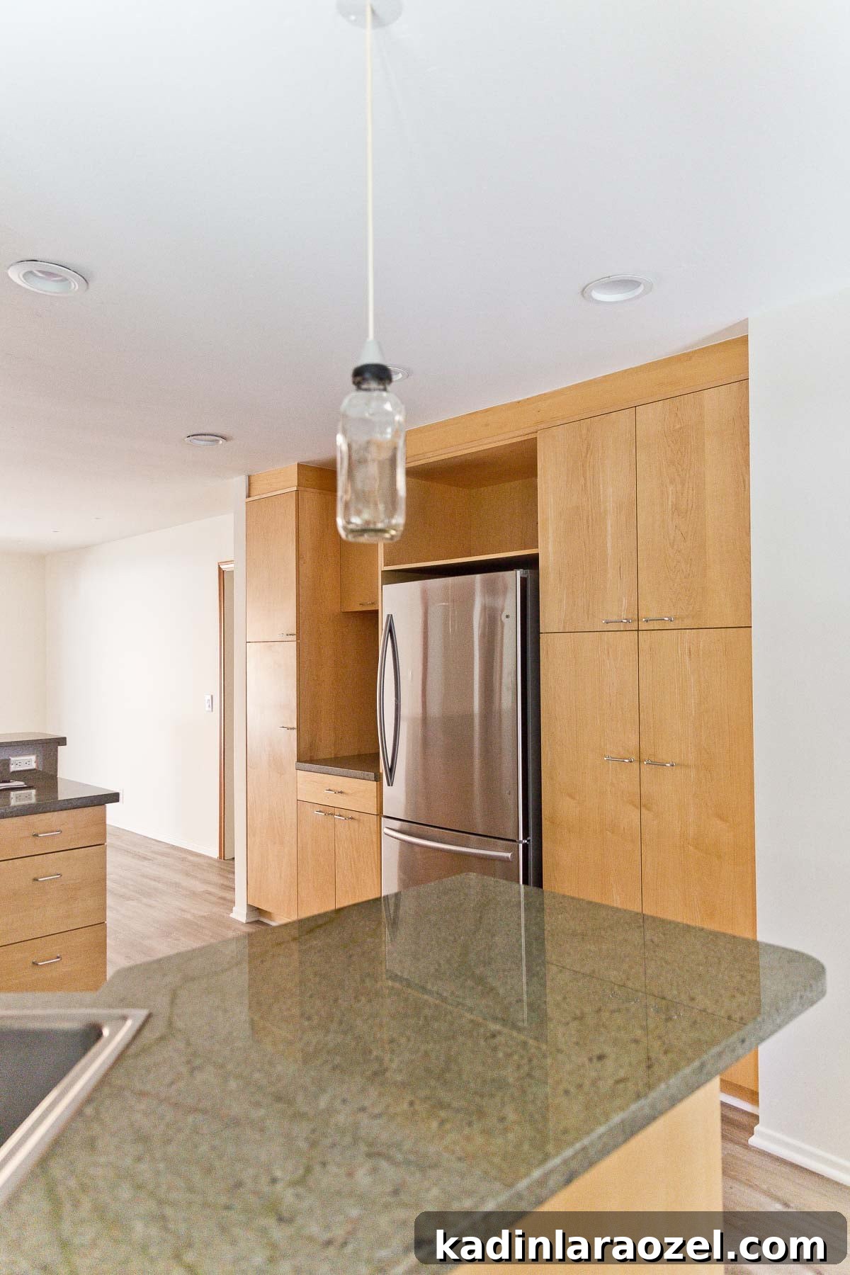 Image of empty kitchen with minimal wood cabinets and green natural stone counters.