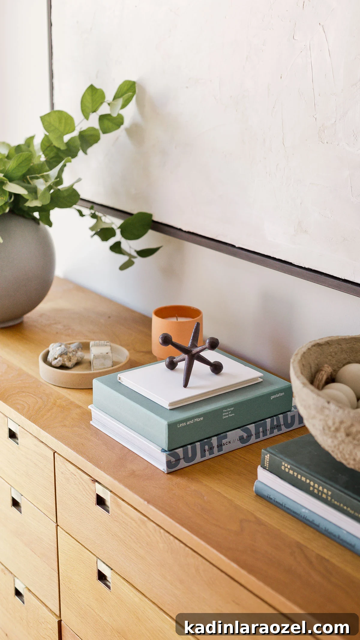 Wood dresser packed with books, home accessories, and a large round vase with fresh greenery