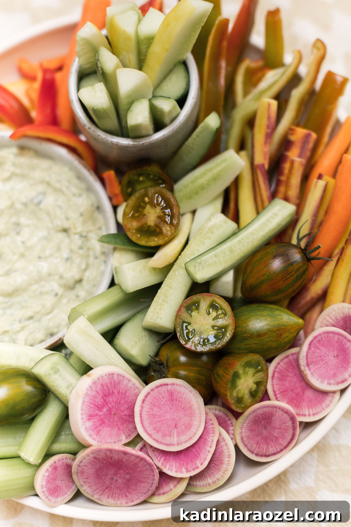 Watermelon radishes, rainbow carrots, cucumbers and hummus laid out of a platter
