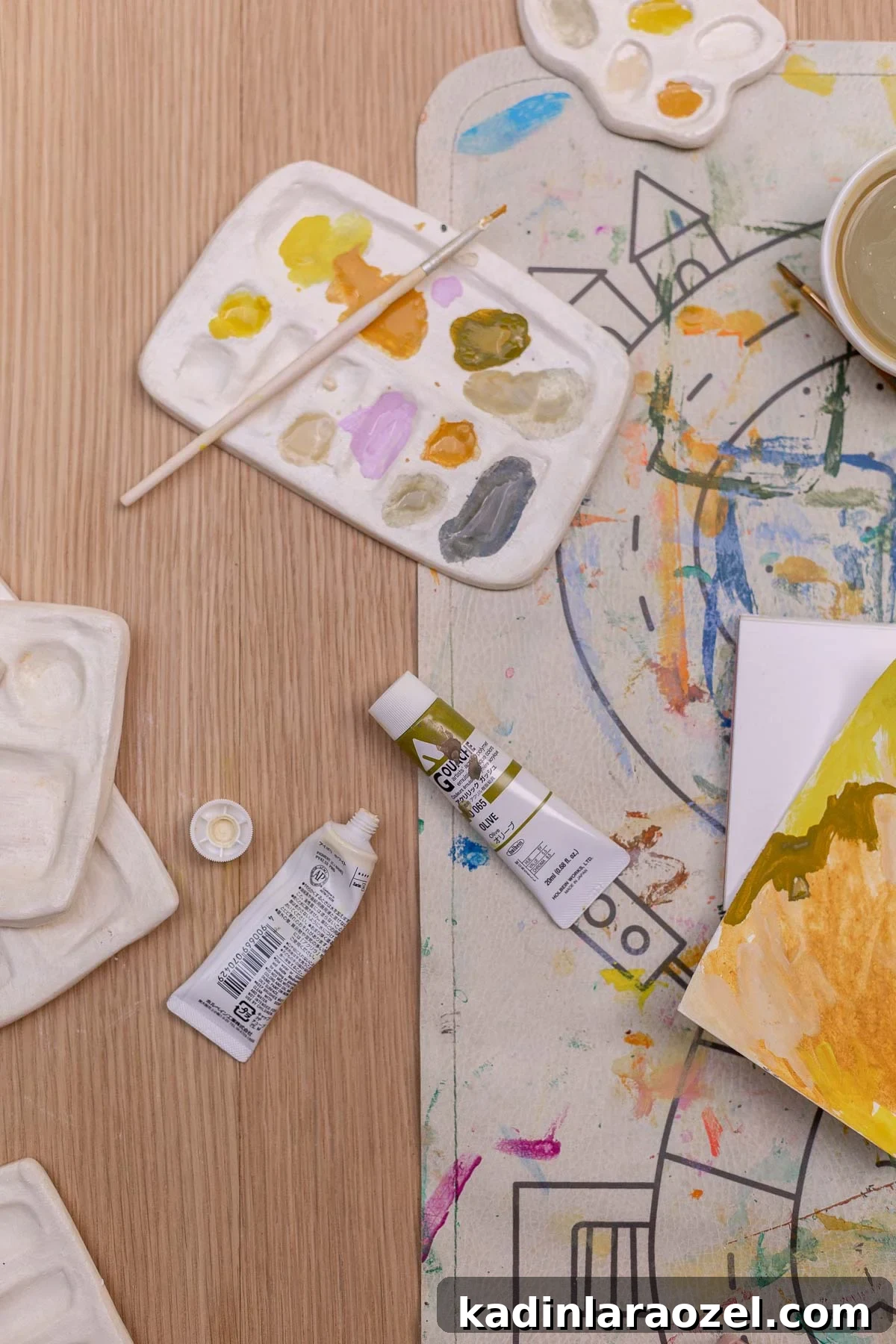handmade paint palette with pastel paints on it, sitting on wood table amongst art supplies