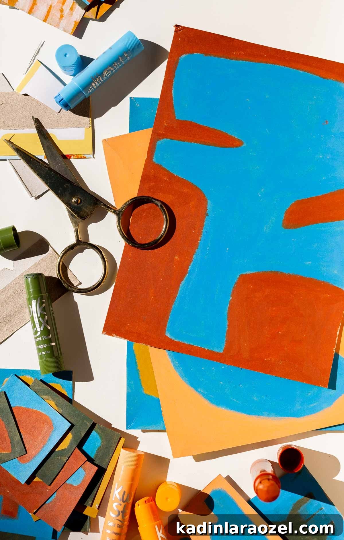 Red and blue artwork stacked on top of other DIY art on a table with art supplies