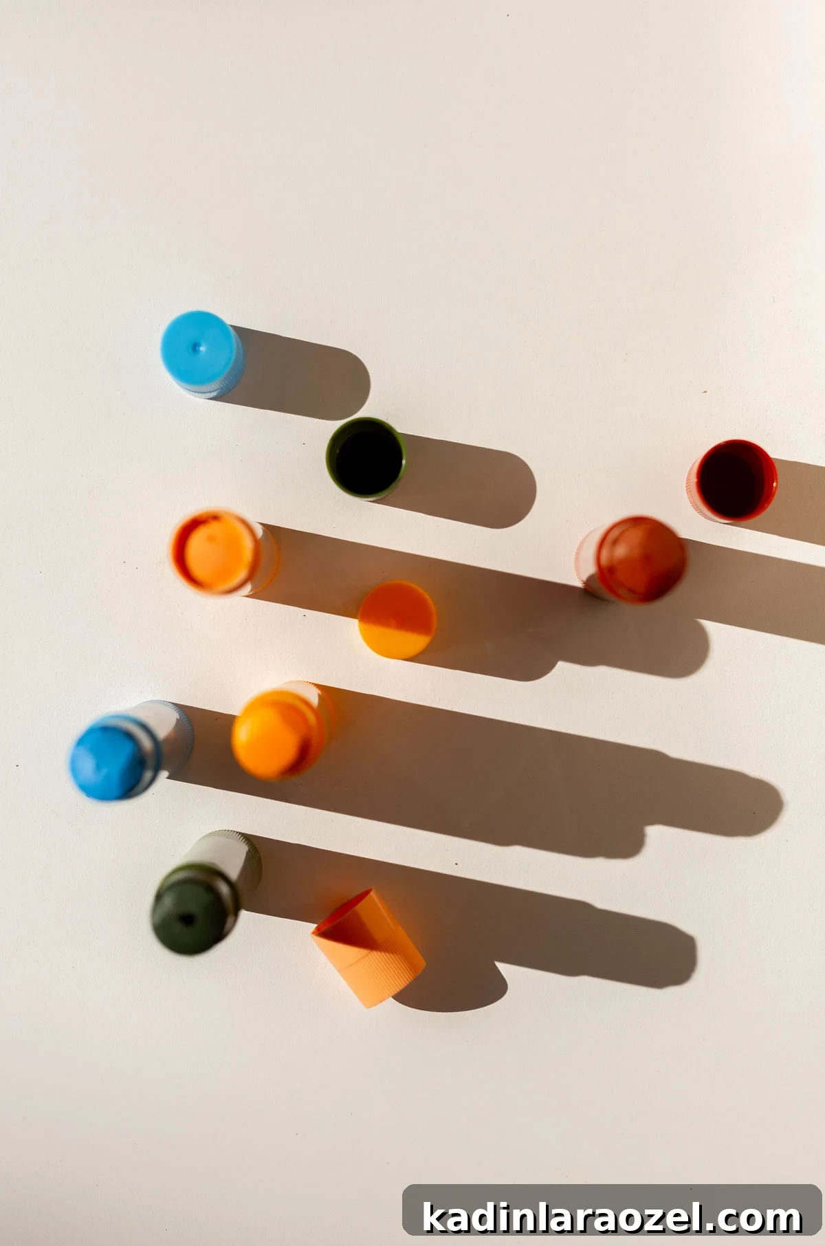 Tempera paint sticks in various colors with a dramatic shadow on white table