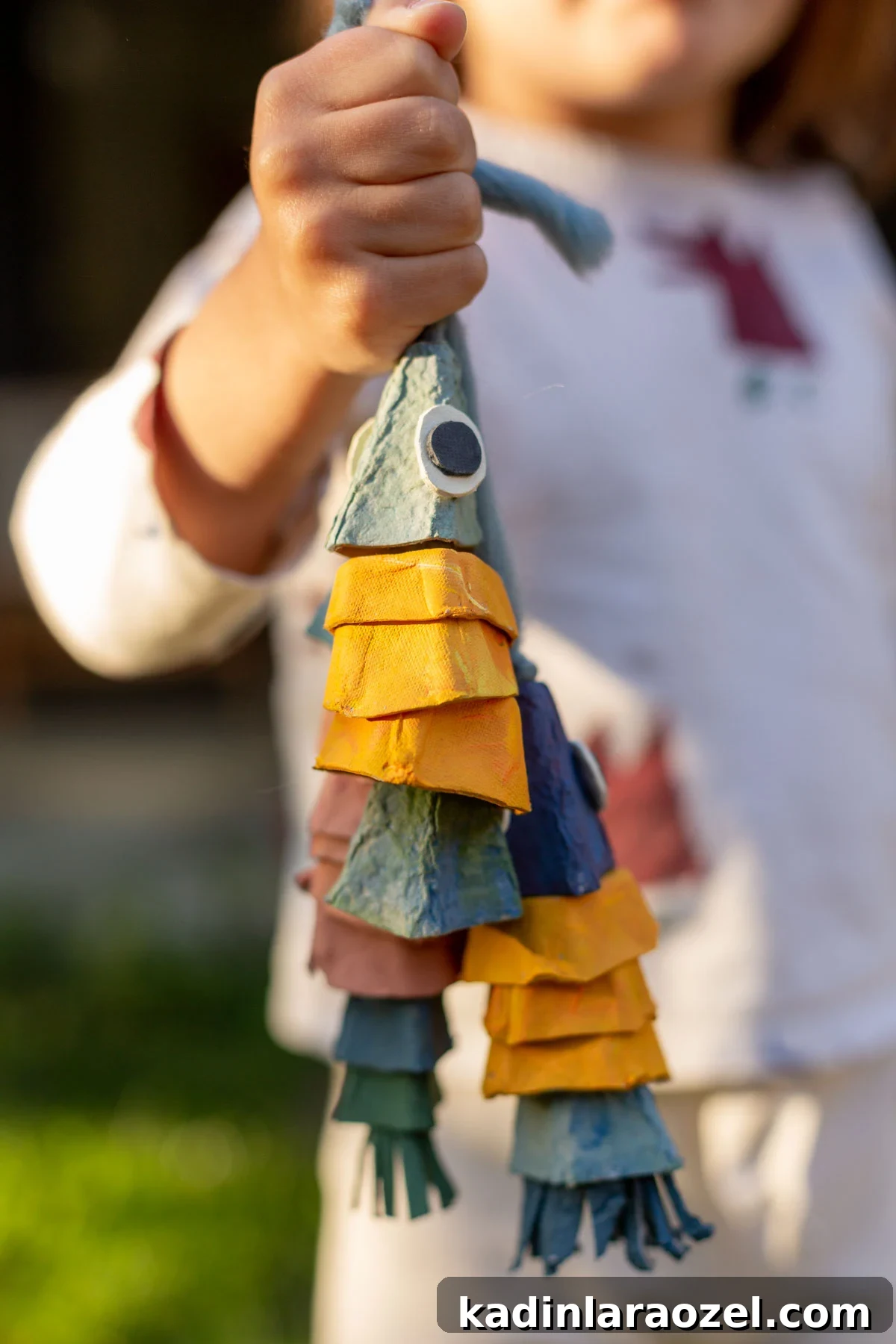 DIY Egg Carton Fish Craft: Make Colorful Fish from Egg Cartons for Kids 4 Child wearing white shirt, holding colorful fish made of egg cartons
