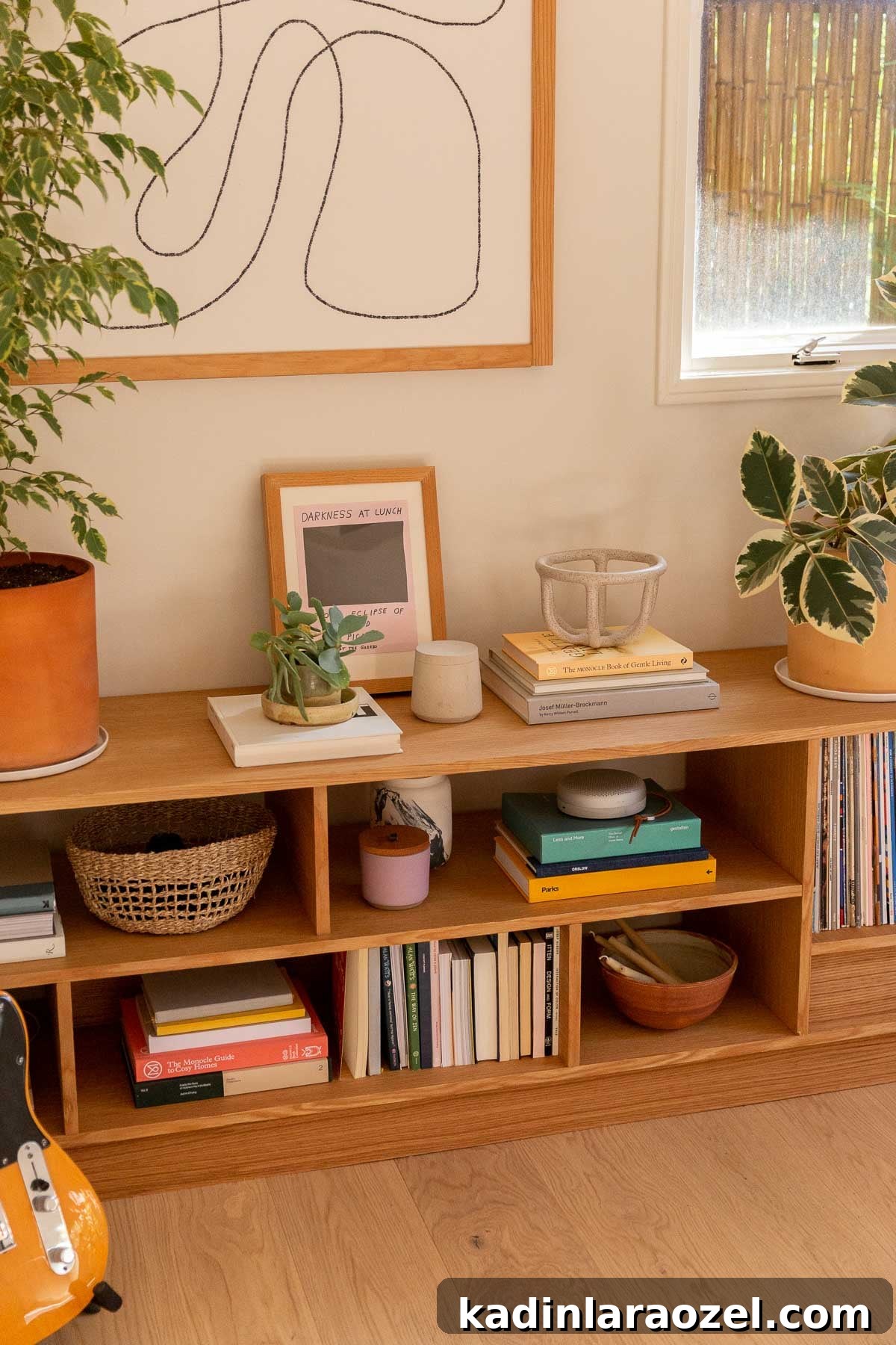 Wood bookshelves against the wall of a white room with stacked books, pottery, and records