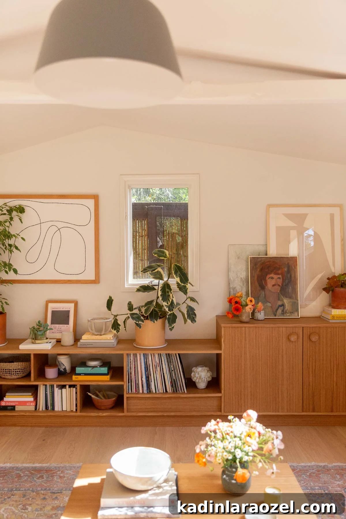 Warm wood cabinetry with open shelving that holds books, plants, and artwork