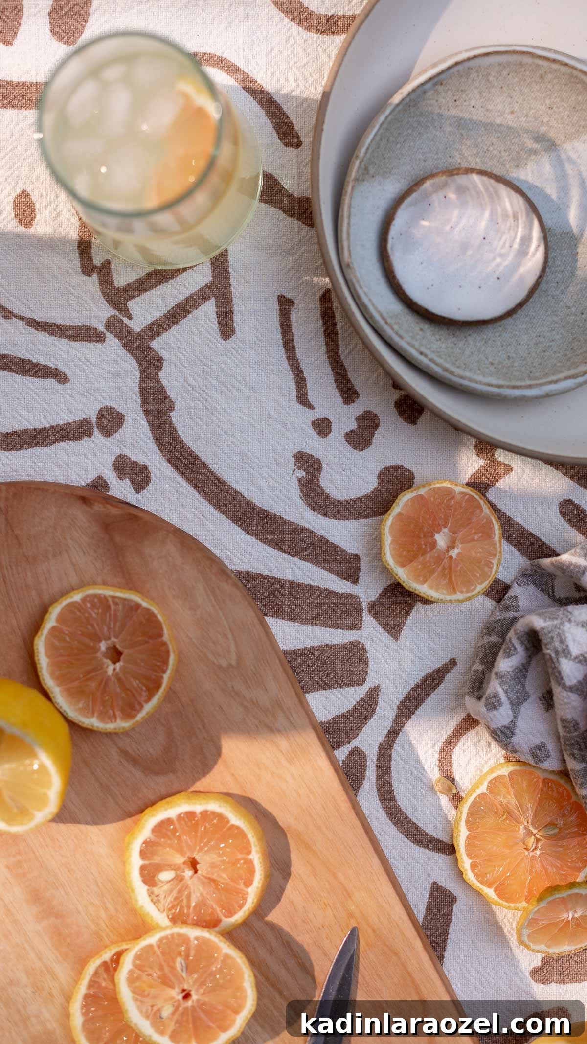 Sliced lemons and oranges on a wood cutting board with a patterned tablecloth and ceramic dishes
