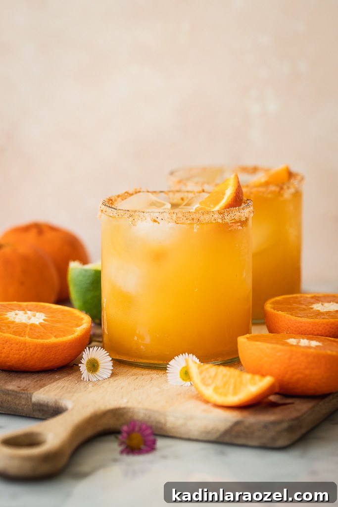 17 Refreshing Summer Cocktails to Try Now 7 orange margaritas in short glasses with orange garnish, sitting on wood cutting board in a kitchen